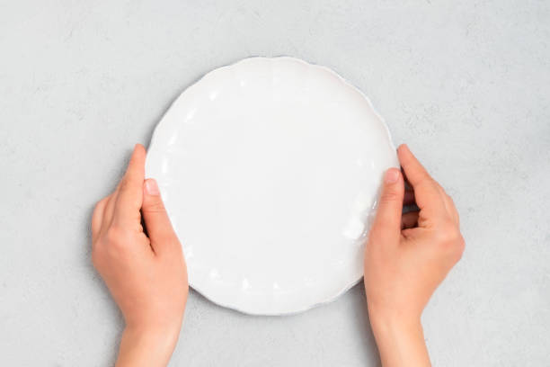 istock Young woman hands holding white empty plate 1214988559