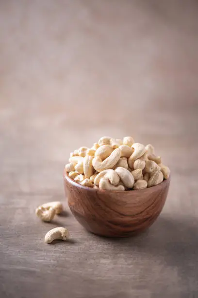 Photo of Cashew nuts in wooden bowl on wood textured background. Copy space. Superfood, vegan, vegetarian food concept. Macro of walnut texture, selective focus. Healthy snack