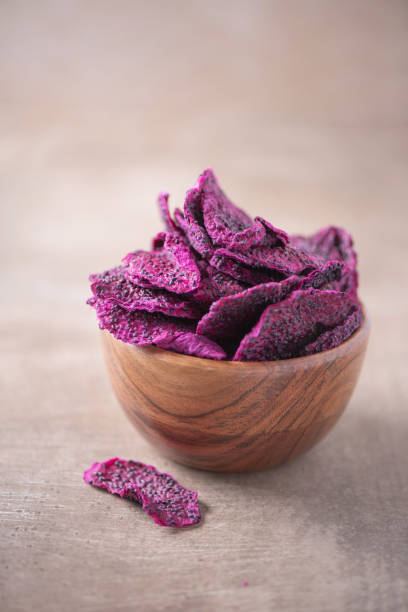 Dried slices of pink dragon fruits, pitaya in wooden bowl on wood textured background. Copy space. Superfood, vegan, vegetarian food concept. Macro of pitahaya, texture, selective focus. Healthy snack. stock photo