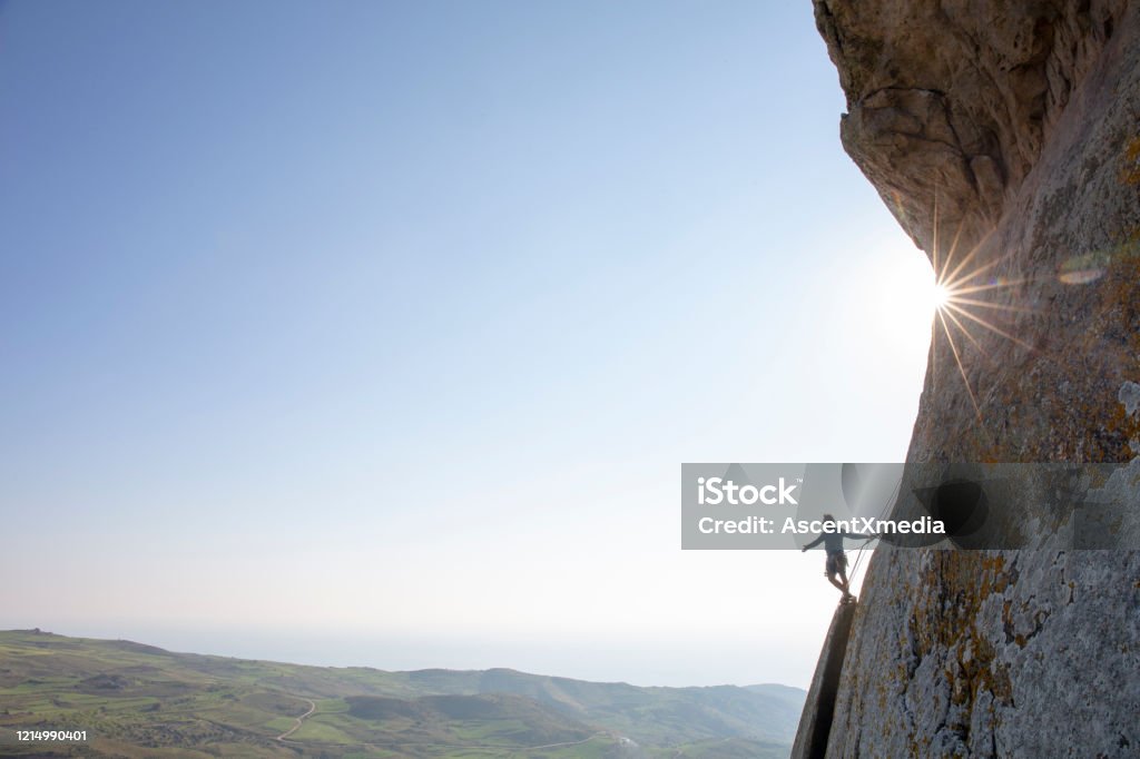Mountain climber ascends rock face at sunrise He looks off to distant scene Large Stock Photo