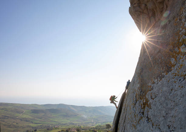 gli alpinisti salgono sulla parete rocciosa all'alba - conquering adversity mountain hiking mountain climbing foto e immagini stock