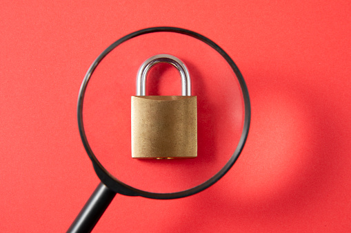 Padlock with magnifying glass on red background