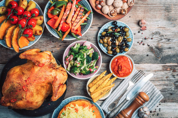 istock Thanksgiving dinner cooking preparation. Traditional dishes: chicken, pumpkin, corn, vegetables salads over wooden background. Top view, copy space. Autumn harvest, organic vegetables. Family dinner 1214992525