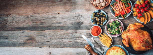 pollo o tacchino intero arrosto, zucche, mais e verdure da raccolta con coltello da cucina e posate servite intorno a tagliere in legno invecchiato su sfondo rustico scuro, telaio. cibo del giorno del ringraziamento - vegies corn dinner crop foto e immagini stock