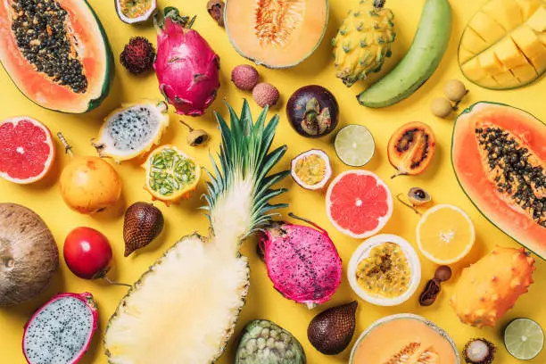 Tropical fruits concept. Exotic fruits - pineapple, papaya, mango, annona, banana, pitahaya, kiwano, african horned melon, tamarillo fruit, granadilla, salak, snake fruit, maracuya, rambutan, lychee, longan, tamarind, mangosteen on yellow background. Top view. Copy space