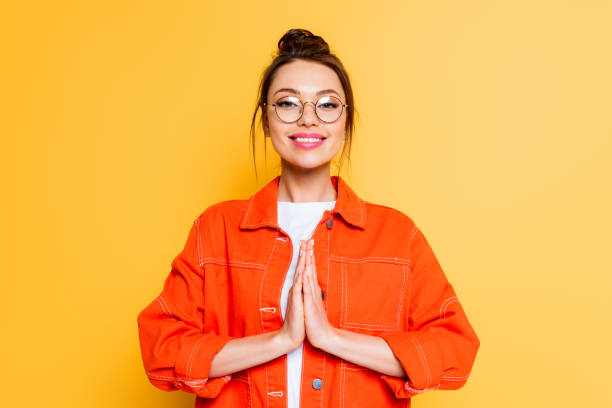 istock smiling student in eyeglasses standing with praying hands isolated on yellow 1214995538