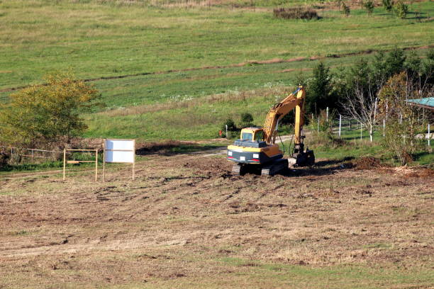 Freshly flattened and cleaned local construction site with single excavator parked after work surrounded with partially dry grass and small trees