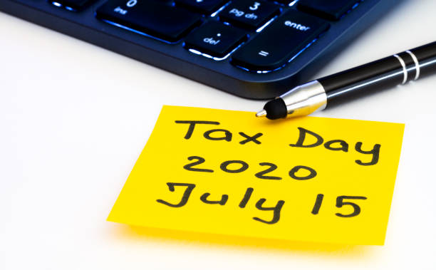 Tax day postponed by american government to July 15th 2020. Tax reminder concept with yellow sticky note, illuminated computer keyboard and pen on white background. Due taxes in United States stock photo