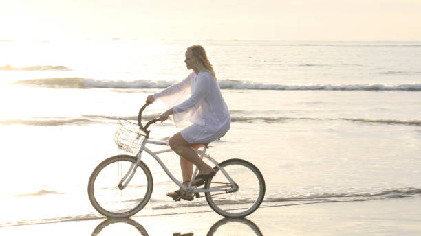 istock Woman bikes along tropical beach at sunrise 1215002493
