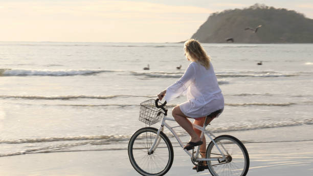 istock Woman bikes along tropical beach at sunrise 1215002521