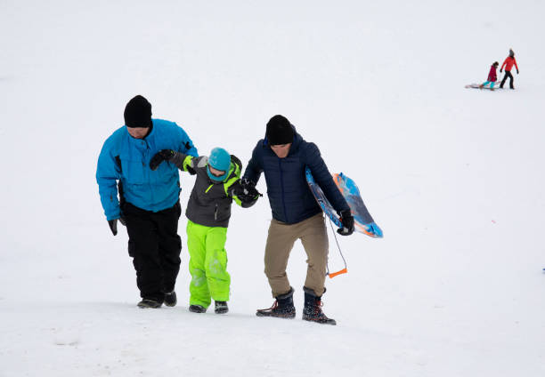 two men help small child hike up toboggan hill - 16705 imagens e fotografias de stock