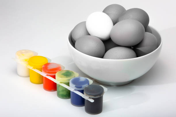 Child hands coloring eggs for Easter holiday. Cups of liquid dye and an egg carton on a white tablecloth