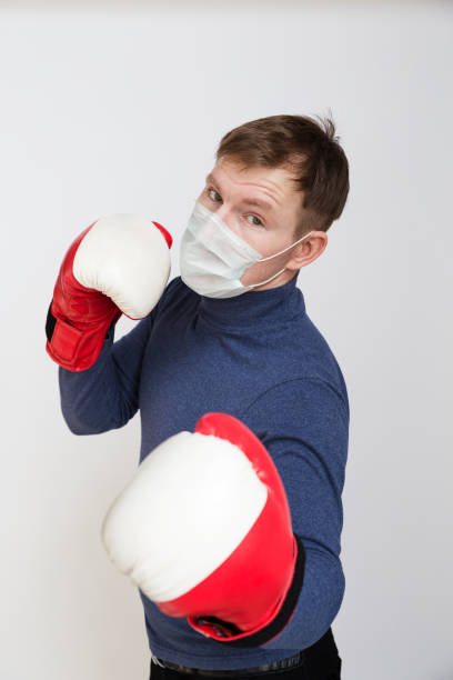 young man in boxing gloves strike. he has a medical mask on his face that protects against infection, viruses, pollution, and coronavirus. - immune defence fotos imagens e fotografias de stock