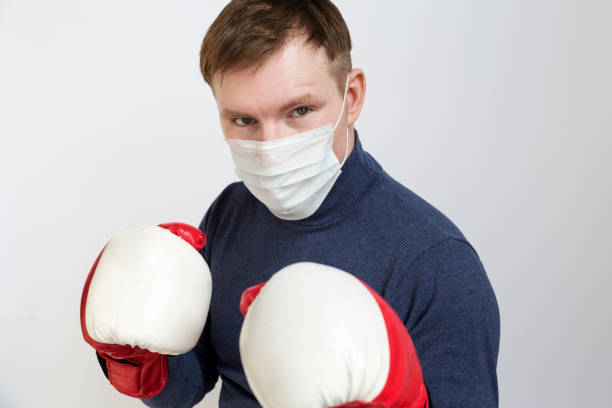 young man in boxing gloves on a white isolated background. he has a medical mask on his face that protects against infection, viruses, pollution and coronavirus. - immune defence fotos imagens e fotografias de stock