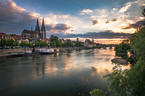 View from Danube river towards Regensburg Cathedral and Stone Bridge in Regensburg, Germany during twilight hours and evening illumination with beautiful water reflections. Shot on Canon EOS full frame system.
