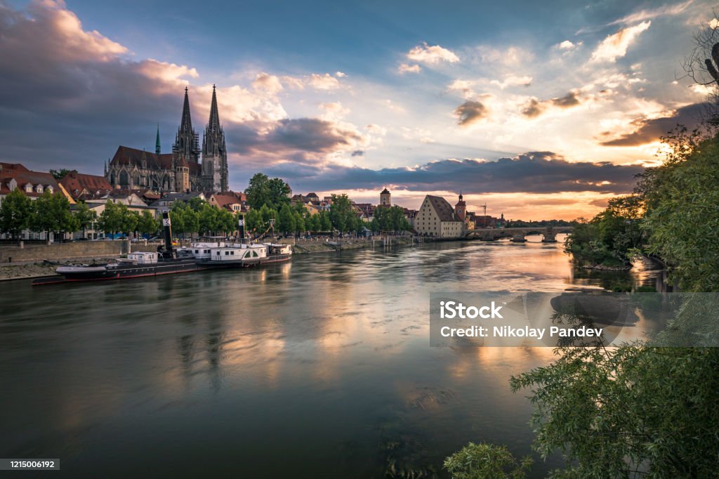 Historical Stone Bridge and Danube river in Regensburg, Germany - Creative Stock Image View from Danube river towards Regensburg Cathedral and Stone Bridge in Regensburg, Germany during twilight hours and evening illumination with beautiful water reflections. Shot on Canon EOS full frame system. Regensburg Stock Photo