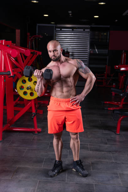 istock Powerful muscular man doing biceps exercise with dumbbell at the gym 1215008829