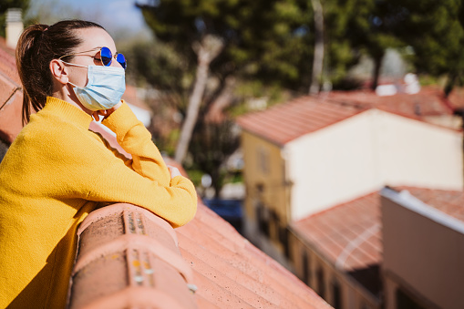 joven en casa en una terraza con máscara protectora y disfrutando de un día soleado. Virus Corona Concepto Covid-19 photo