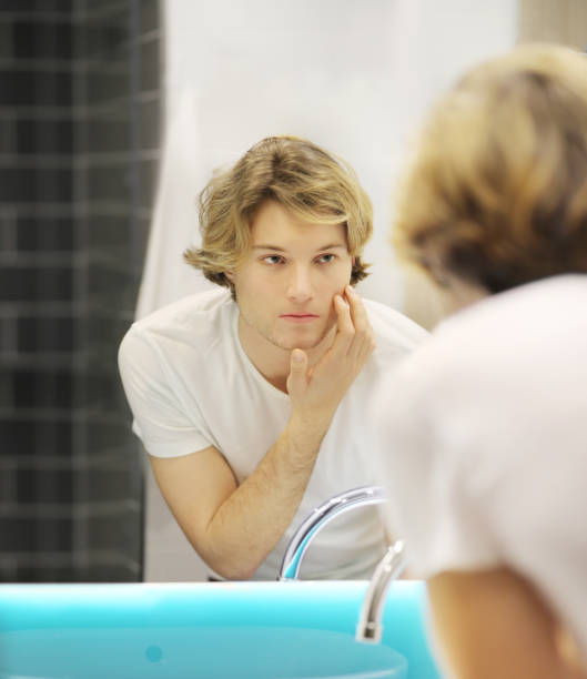 istock young man looking in the mirror,combing his hair,looking at problems on face 1215010227