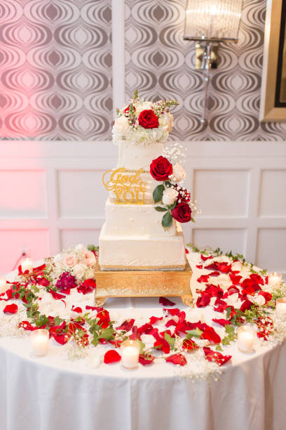 Elegant Wedding Cake A classic and elegant white tiered Wedding Cake on a gold cake stand with red & white roses all over it. Cake has a gold sign on it with the words "God gave me you." white wedding cake red roses stock pictures, royalty-free photos & images