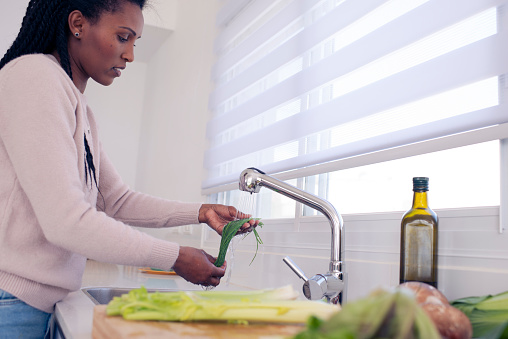 Close up young African woman washing scallion under faucet in the kitchen.