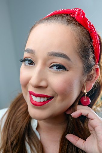 A portrait of a young woman smiling to the camera with a red lipstick and casual makeup on.