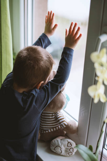 istock Small boy with stuffy toy in protective medical masks looking through a window . Prevention epidemic 1215014059