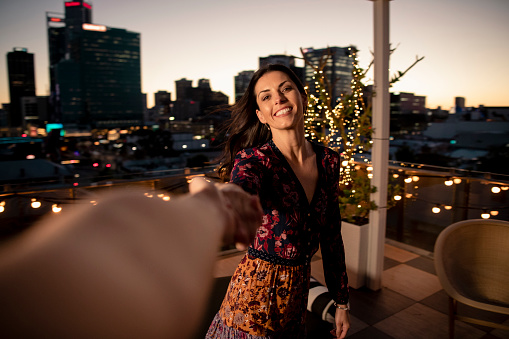 A personal perspective of a woman dancing with an unrecognisable person while holding their hand on a hotel rooftop in Perth, Australia at dusk.