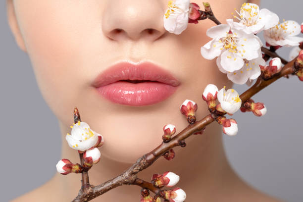 jeune fille avec le beau maquillage nu et les lèvres dodues. les lèvres naturelles parfaites se ferment vers le haut. près d’elle sont belles fleurs de printemps fleuris sakura. maquillage professionnel et soins de la peau de cosmétologie. - cherry blossom flower head spring flower photos et images de collection