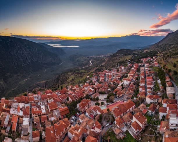 aerial view of delphi, greece, the gulf of corinth, orange color of clouds, mountainside with layered hills beyond with rooftops in foreground - gulf of corinth imagens e fotografias de stock