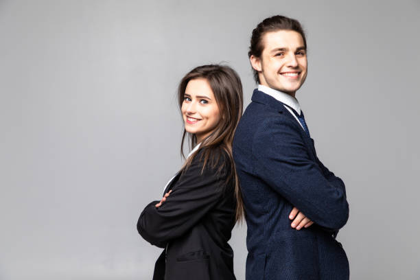 istock Two young business people standing back to back with hands crossed isolated on grey background 1215025044