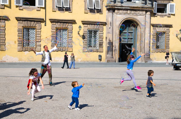 Lucca, Italy, September 14, 2018: man is blowing colorful soap bubbles and playing with small young children on Napoleone square near Palazzo Ducale palace in historical centre of medieval town Lucca Lucca, Italy, September 14, 2018: man is blowing colorful soap bubbles and playing with small young children on Napoleone square near Palazzo Ducale palace in historical centre of medieval town Lucca lucca italy stock pictures, royalty-free photos & images