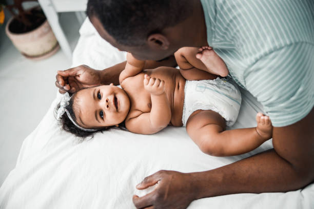 Adorable Afro American baby lying on bed with daddy Loving father spending time with cute newborn daughter at home stock photo adult diaper stock pictures, royalty-free photos & images