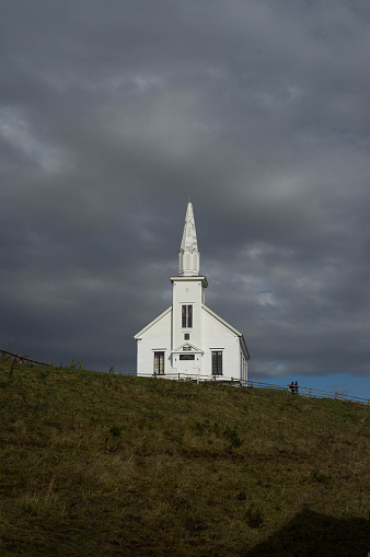 Iona, Nova Scotia, Canada.  October 15, 2018.  A white church on a hill with dark skies overhead.  Two people stand on the hill near the church.