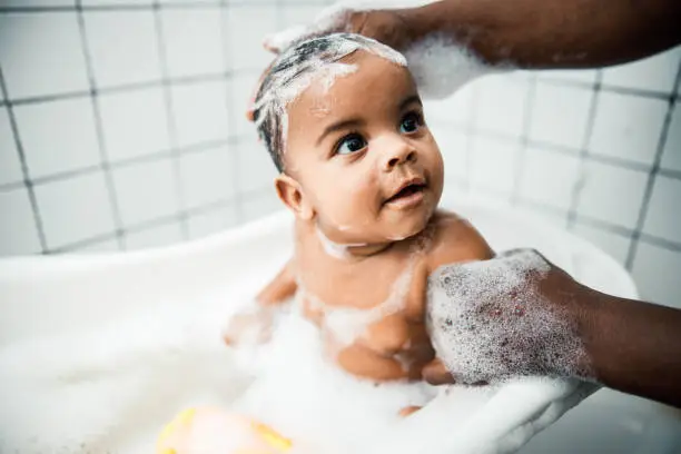 Photo of Afro American man washing hair of adorable newborn child