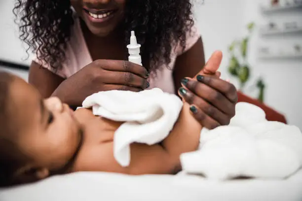 Close up of cute newborn girl lying in bed while mother holding nasal drops stock photo