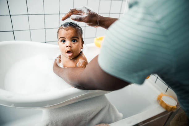 Loving father washing hair of his adorable newborn daughter Afro American man bathing cute toddler baby in bathroom at home stock photo taking a bath photos stock pictures, royalty-free photos & images