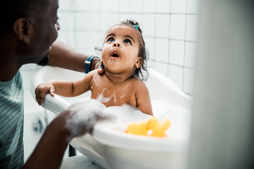 Adorable Afro American baby taking bath with daddy stock photo