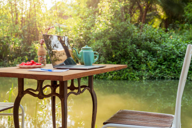istock Laptop computer with tea mug and rose apple fruit on wood table by the canal. 1215038516