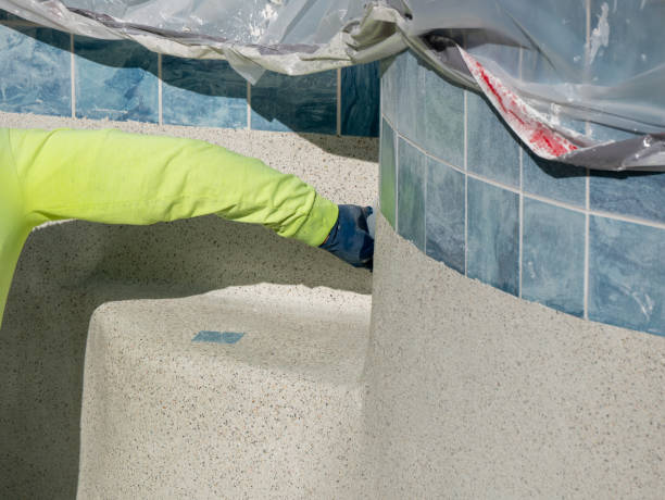 istock Man using a plastic trowel to smooth and shape newly applied textured cement containing pebbles on a swimming pool 1215040554