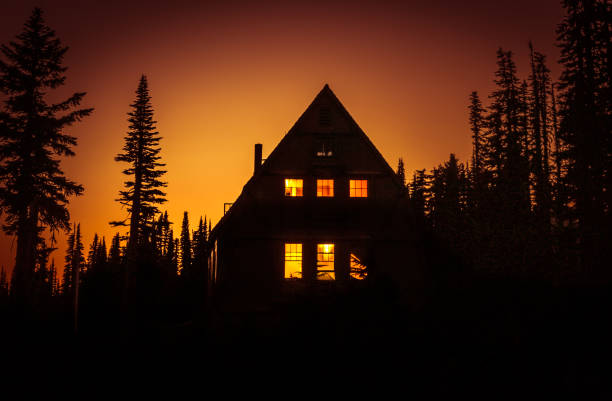 View of cabin in the woods with lit windows at sunset