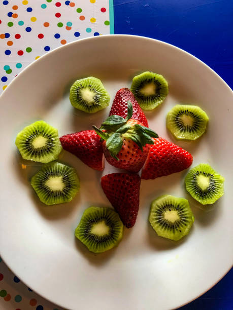 istock Sliced kiwi and whole strawberries on white plate 1215043743