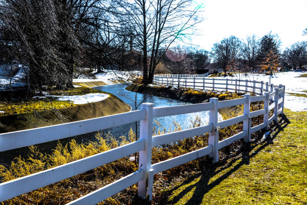 A view of Weasel Brook Park in Clifton, New Jersey during the winter with the brook crossing through the park behind a white wooden fence. Clifton in one of the townships that conform Passaic County in New Jersey.