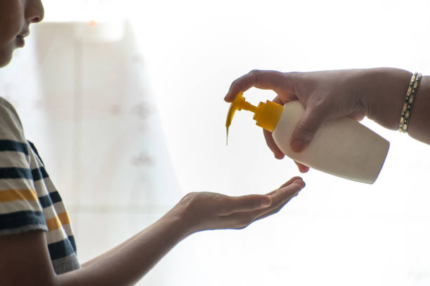 mother applying liquid soap on hand of 11 year old boy