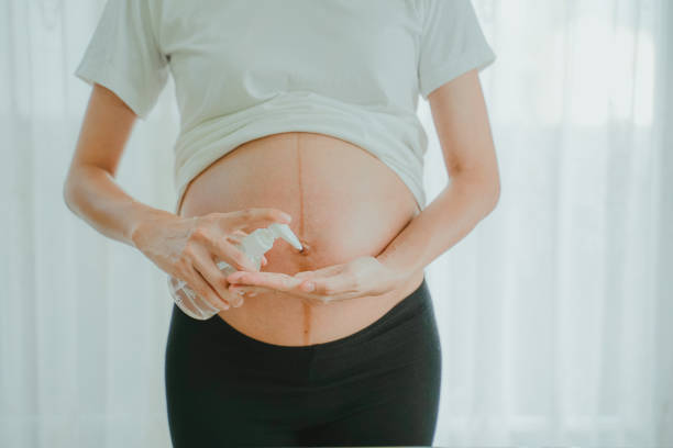 A pregnant woman wears a surgical mask is washing hands by alcohol gel on the sofa. Protect a COVID-19 (Coronavirus), PM 2.5 and prevent infection to the fetus concept. stock photo