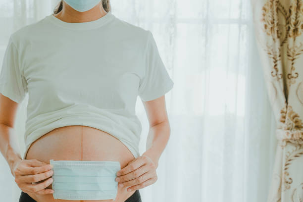 A pregnant woman wears a surgical mask to protect a COVID-19 (Coronavirus) and PM 2.5 and show a surgical mask on the abdomen to prevent infection to the fetus. stock photo