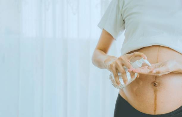 A pregnant woman wears a surgical mask is washing hands by alcohol gel on the sofa. Protect a COVID-19 (Coronavirus), PM 2.5 and prevent infection to the fetus concept. stock photo