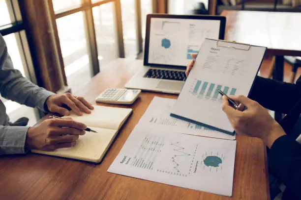 Photo of Two business partnership coworkers analysis strategy with discussing a financial planning graph and company budget during a budget meeting in office room.