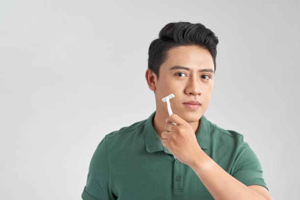 istock Handsome young man shaving his face and looking at camera while standing isolated on grey background 1215054855
