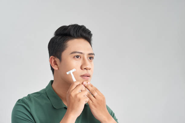 istock Young man is passing the razor for the beard while it looks at the mirror 1215055407
